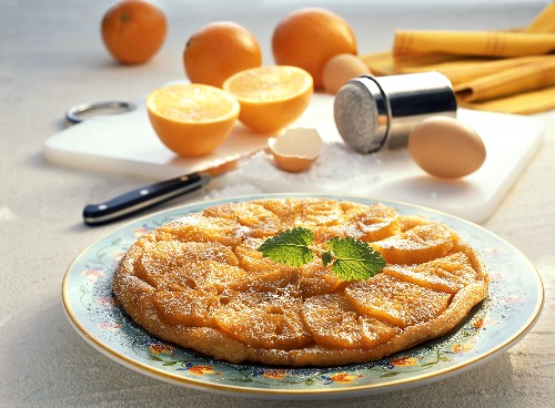 Orangen-Tarte mit Puderzucker auf Teller vor Zutaten