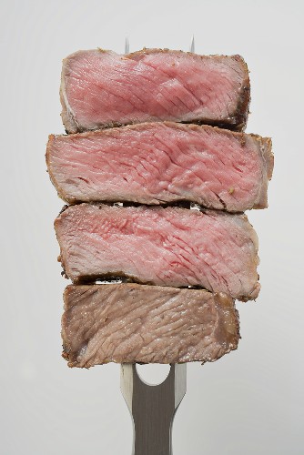 Slices of beef steak on carving fork (different degrees of cooking)