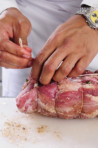 A pork shoulder joint being rolled up and tied with kitchen twine