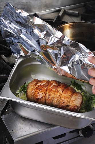 Pork roulade in a roasting tin being covered with aluminium foil