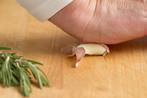 A hand crushing a garlic clove