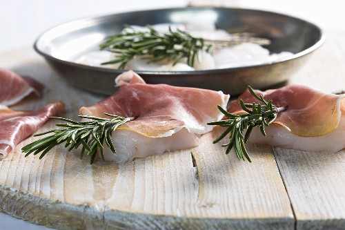 Fish medallions with ham and rosemary being prepared
