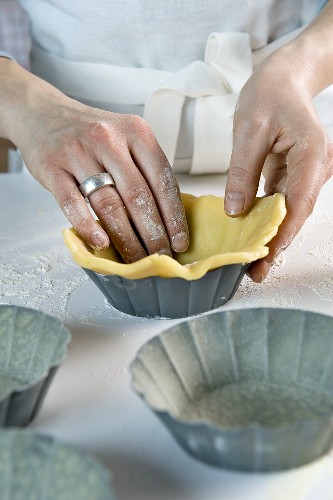 Shortcrust pastry being placed into baking tins