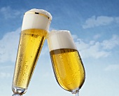 Two Clinking Beer Glasses Against a Blue Sky