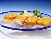 Four breaded fish slices with fresh parsley& lemon wedge on glass plates