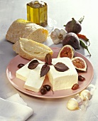 Piece of feta on plate with figs, olives & white bread