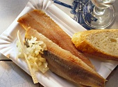 Two matje herrings with chopped onions & bread on paper plate