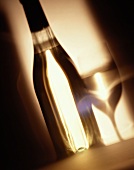 Weinflasche ohne Etikett nebem Glas vor braunem Hintergrund