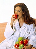 Rothaarige Frau in weißem Bademantel beisst in roten Apfel