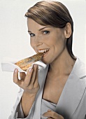 Junge Frau in weißem Blazer isst ein Stück Pizza