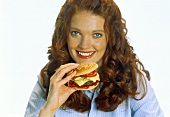 Rothaarige Frau in blauer Bluse isst einen Hamburger