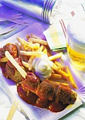 Skewered curry sausage with fries and mayonnaise on paper plate with Glass of Beer