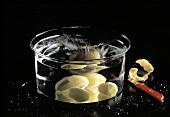 Rohe geschälte Kartoffel fällt ins Wasser einer Glasschale