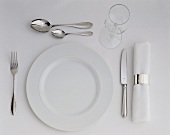 A place setting with white plate, cutlery, napkin & wine glass