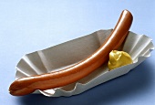 A sausage with mustard in paper tray
