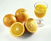 Drei Orangen (eine halbiert) & ein Glas Orangensaft