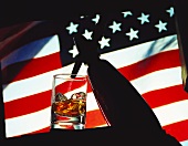 Glas Whiskey-Soda mit sprühender Sodaflasche vor USA-Flagge