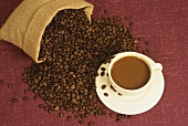 Cup of coffee with milk, coffee beans falling out of sack