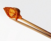 Wooden chopsticks holding a deep-fried won ton (pastry parcel)