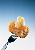 Ein Stück gegrillter Maiskolben mit Butterröllchen auf Gabel