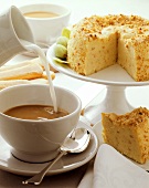 Cup of coffee with milk being poured into it & almond cake