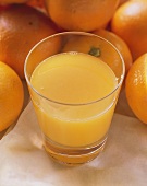 Ein Glas Orangensaft vor vielen frischen Orangen