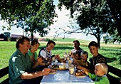 German family having afternoon snack under trees in field