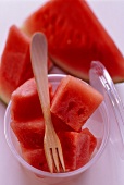 Watermelon pieces with wooden fork in plastic tub