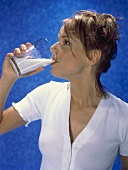Junge Frau trinkt ein Glas Milch, blauer Hintergrund