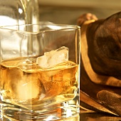 Ein Glas Whisky mit Eiswürfeln & Whiskyflasche im Hintergrund