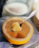 Piece of grapefruit on spoon above yellow grapefruit half