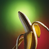 Halb geschälte Banane vor rot-grünem Hintergrund
