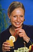 Junge Frau hält ein Glas Multivitaminsaft mit Strohhalm