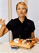 Young blond woman eating sushi with chopsticks