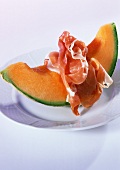 A piece of netted melon with raw ham on plate