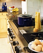 View into a kitchen with blue pan on stove, eggs, noodles