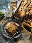 Moussaka in cooking dish and on plate; Ouzo bottle