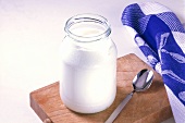 Natural yoghurt in jar on kitchen board, silver spoon