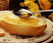 Honey running from spoon on to a roll, flowers behind