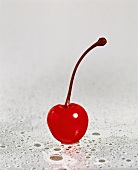 A cocktail cherry on sheet of glass with drops of water