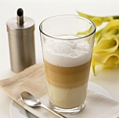 A glass of latte macchiato in front of a sugar sifter
