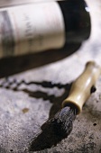 A corkscrew on stone surface in front of red wine bottle