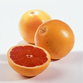 Half a pink grapefruit in front of two whole ones