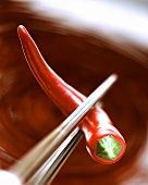 Chopsticks holding a red chili pepper
