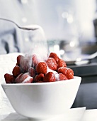 Sprinkling sugar on a bowl of fresh strawberries