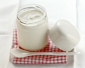 A jar of yoghurt with plastic spoon on checked cloth