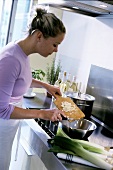 Young woman putting chopped vegetables into metal dish