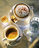 Espresso, Cappuccino, Glas Wasser und Würfelzucker