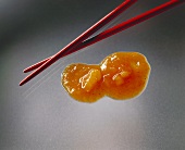 A blob of Chinese sauce on sheet of glass, chopsticks beside it