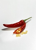 Two red chilis, one cut open with seeds